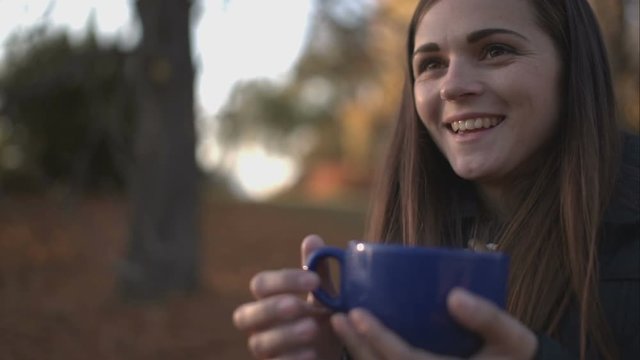 Woman drinking tea in the park in autumn.