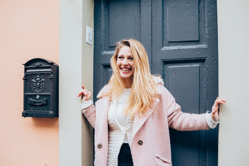 Obraz premium young beautiful caucasian blonde hair woman standing on the front door, overlooking smiling - happiness, having fun, smiling concept