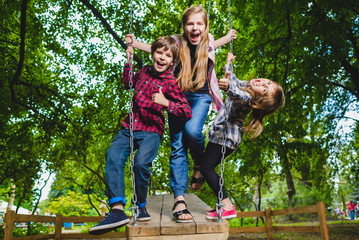 Smiling kids having fun at playground. Children playing outdoors in summer. Teenagers riding on a...