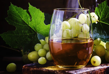 White wine in a glass, green grapes with leaves in a wine cellar