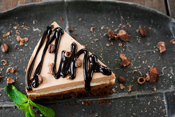 Cocoa sweet cheesecake with chocolate sauce on black plate, decorated with mint leaves top view, free space