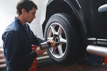 Mechanic changing car wheel in auto repair shop. Closeup of serviceman with tools working near...