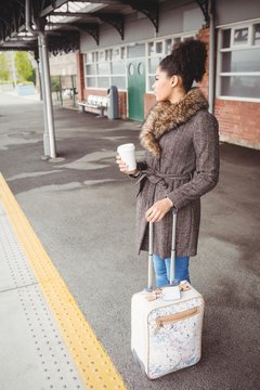 Woman holding disposable coffee cup at railway station platform