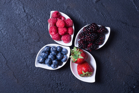 berries : raspberries , blueberries , blackberries , strawberries. Fresh summer berries in a white bowl on a stone background.