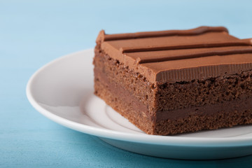 Piece of chocolate cake on white plate on blue background. Selec