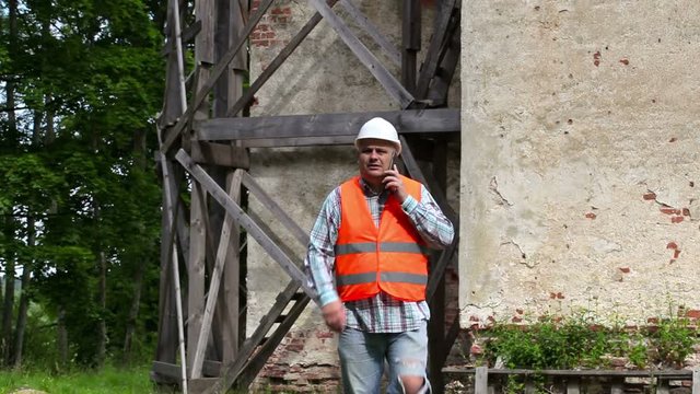 Construction worker walking and talking on smart phone near wooden scaffolding