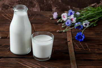Bottle with milk and glass of milk at wooden table.