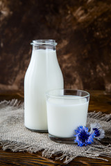 Bottle with milk and glass of milk at wooden table.
