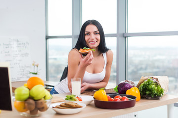 Close-up portrait of smiling woman eating diet vegetarian sandwich with vegetables for breakfast in morning, looking at camera.