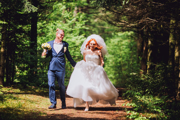 Newlyweds run along the path in the park on the evening. Bride with ore hair