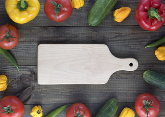 Cutting board and fresh vegetables on wooden table. red and yellow peppers, cucumber chilli and habanero peppers, tomatoes. Image with copy space.