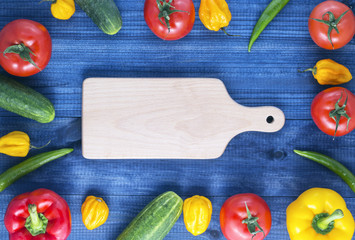 Cutting board and fresh vegetables on wooden table. red and yellow peppers, cucumber chilli and habanero peppers, tomatoes. Image with copy space.