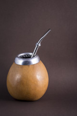 yerba mate in gourd matero with bombilla on brown background