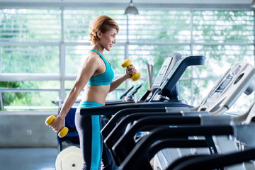 Asian woman walking on treadmill holding dumbbell