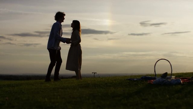 4K Silhouette man proposes at sunset to his girlfriend and she accepts, in slow motion