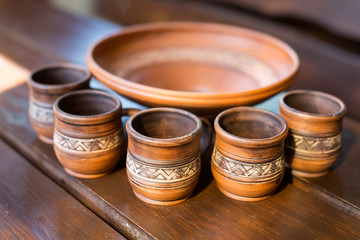 Five cups and a bowl of red clay with Ukrainian ornament on the wooden table closeup