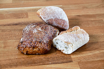 Light and dark bread and buns lying on a table of dark brown laminated hardwood