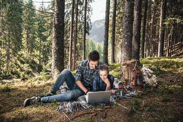 Fototapeta premium A couple of tourists lie on the blanket and looking at laptop in the woods. The concept of active rest
