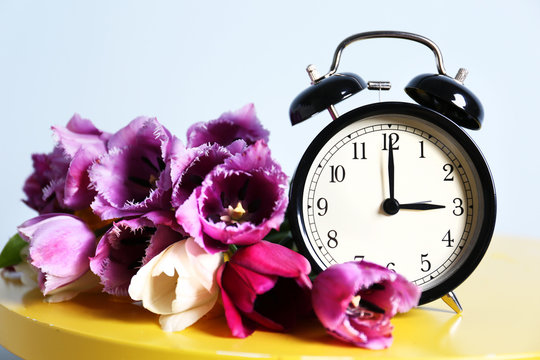 Alarm clock with tulips bouquet on table