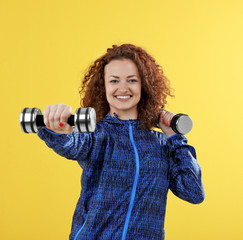 Obraz premium Attractive woman exercising with dumb bells on yellow background