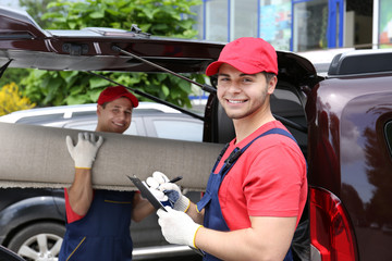 Two male workers unloading carpet from car