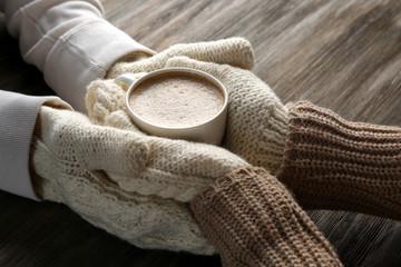 Fototapeta na wymiar Lovely couple holding cup of coffee in knitted gloves on wooden background