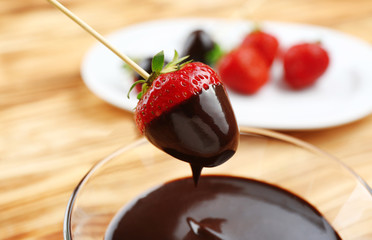 Strawberry dipping into bowl with chocolate on blurred background