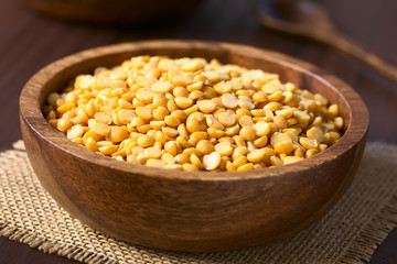 Raw yellow split peas in wooden bowl, photographed on dark wood with natural light (Selective Focus, Focus in the middle of the image)