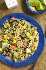Quinoa salad with sweet corn, olive, tomato, cucumber and chives on plate, photographed overhead on slate with natural light
