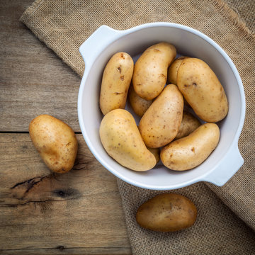 Composition of fresh organic potatoes in white ceramic bowl on h