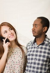 Interracial charming couple wearing casual clothes posing interacting friendly, woman talking on cell phone and man listening in, white studio background