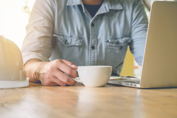 Business man holding a cup of coffee and using laptop, on wooden