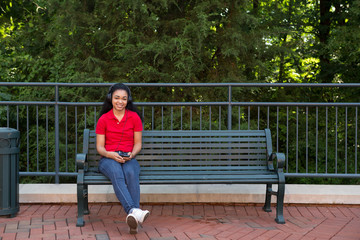Fototapeta premium A young african american college student sitting on a bench with her cell phone