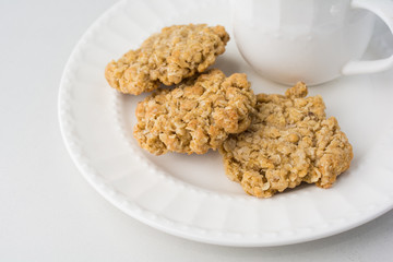 Three oatmeal cookies on white plate with teacup