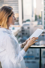 Fototapeta premium Young successful businessman working on table, back view of young woman typing on touch screen of digital tablet, Tablet on city background, Flare light, Shallow DOF.