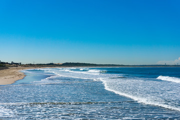 Beautiful ocean beach with moderate surf and broad waves against blue sky with a plane on the background. Cronulla, Australia. Copy space