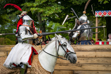 Armored knights on horseback charging in a joust right after the impact . Jousting is a martial...