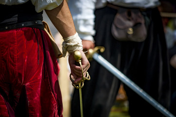 Closeup on the hand holding a sword of a pirate or medieval warrior, preparing to duel another man,...