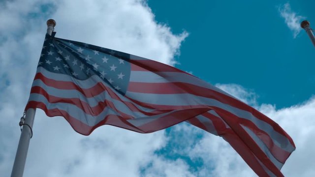 American flag on the flagpole waving in the wind against a blue sky with clouds. Slow motion, high speed camera, 250fps