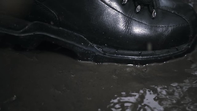 Black new and glossy boots step on a puddle and creates a splash water and dirt which fly around. Slow motion, high speed camera, 250fps