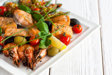 Greek cuisine - traditional grilled seafood plate with shrimps, salmon, olives lemon and cherry tomato on white wooden background