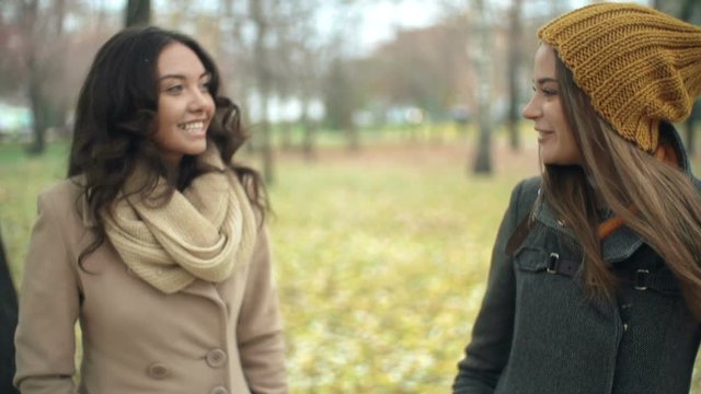 Two beautiful girls walking together in the park, talking and laughing