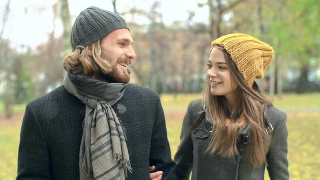 Young loving couple walking in the autumn park and looking at camera with smile