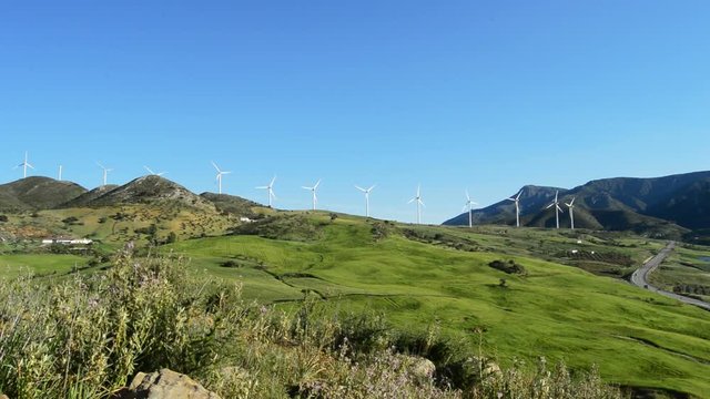 Mountains and green fields with wind turbines energy renewable towers moving at sunny day
