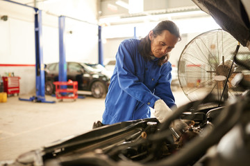 Professional Asian mechanic repairing vehicle in garage