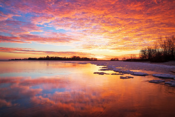 Beautiful winter landscape with sunset fiery sky and frozen lake