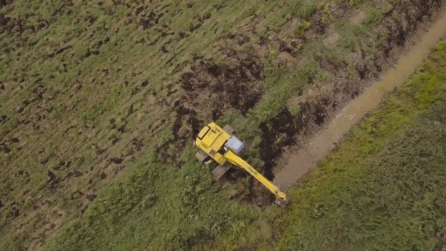 Excavator is digging an irrigation canal.Aerial view:Excavator digging a deep trench.excavator is digging an drainage canal in the agricultural field.4K,UHD.