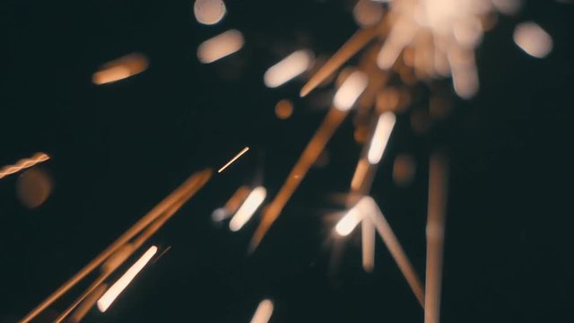 Sparks fly directly into the camera against a black background. Stream of sparks from defocus fly in focus. Slow motion, high speed camera, 250fps