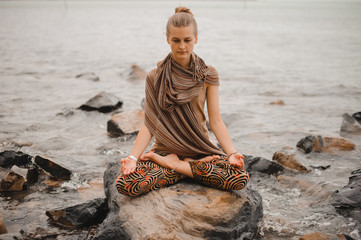 Young woman in lotus pose meditating on rock