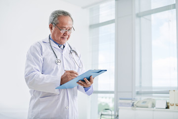 Portrait of experienced Vietnamese doctor making notes